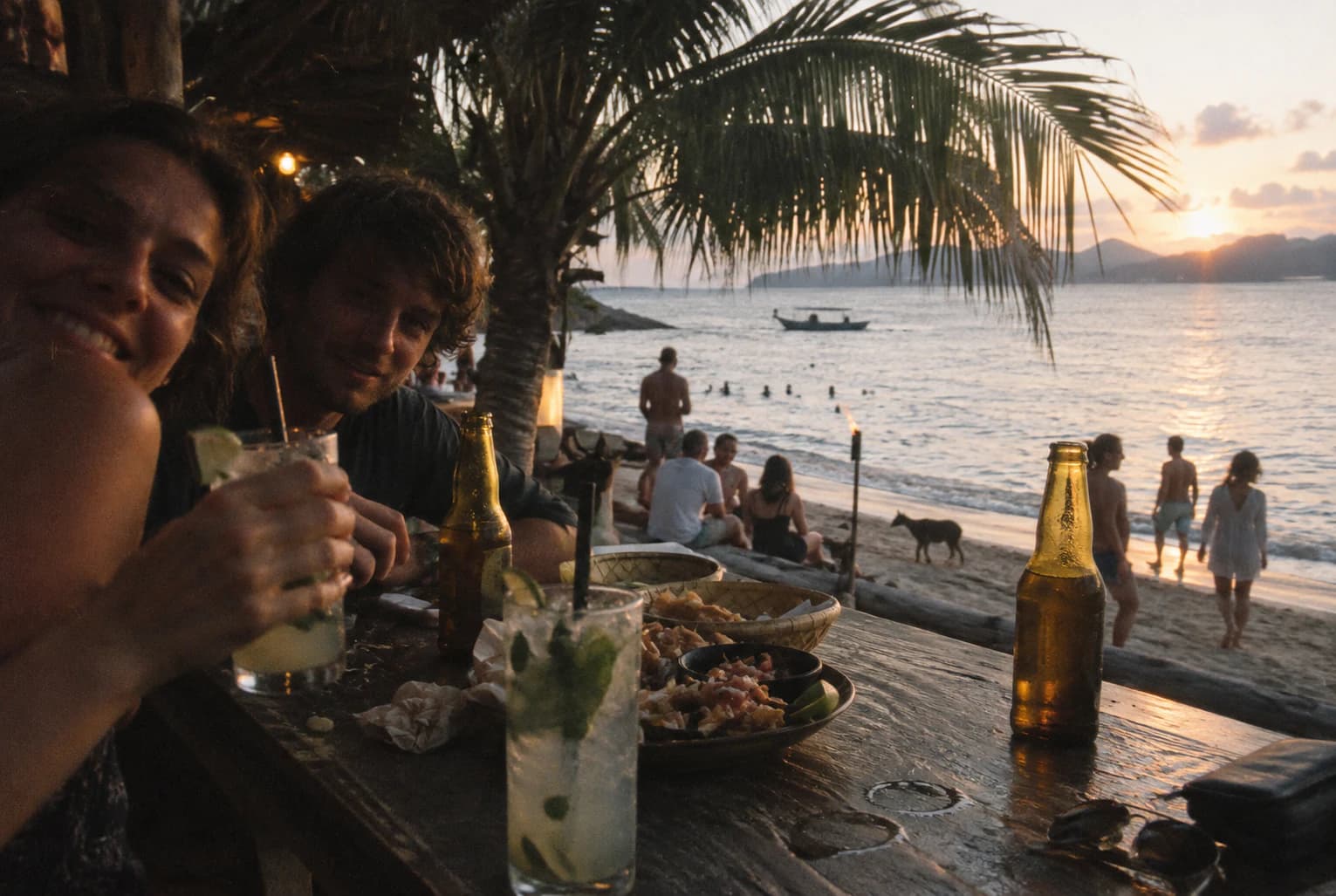 Friends sharing drinks at a beach table near sunset